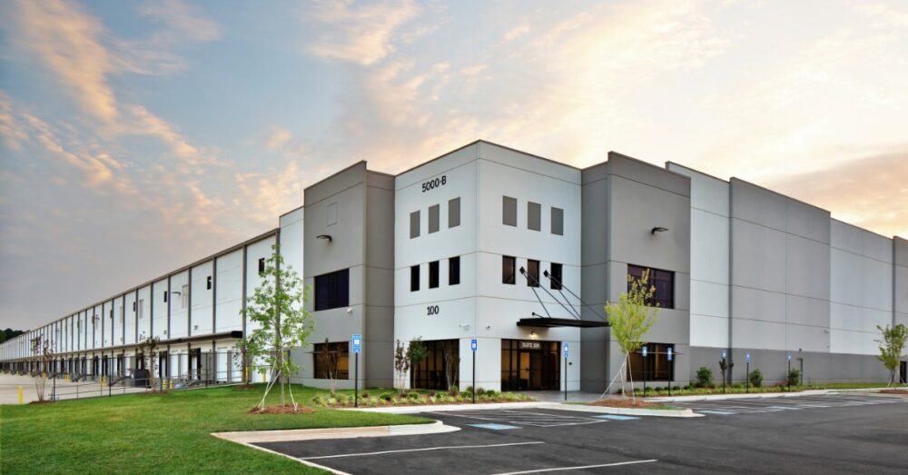 A wide shot of a large warehouse facility from the outside, showing the entrance and loading docks on the side of the building.